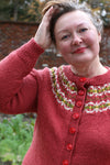 A woman wearing a red cardigan with a decorative yoke in three colours.