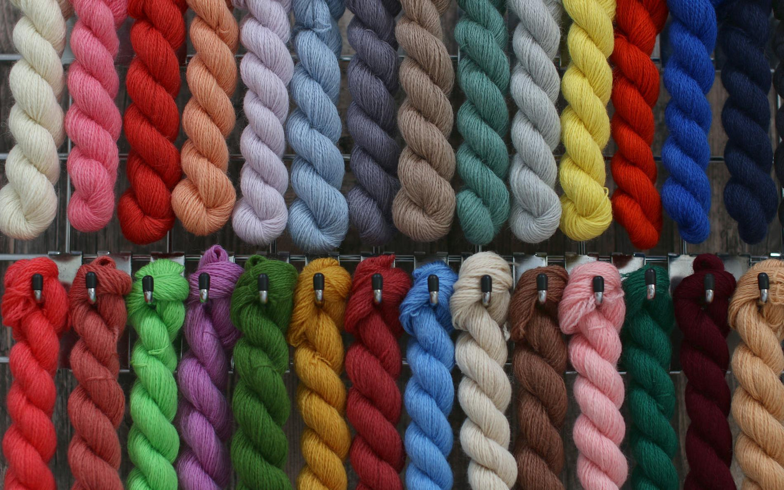 Many skeins of wool all different colours hanging from hooks in two rows.
