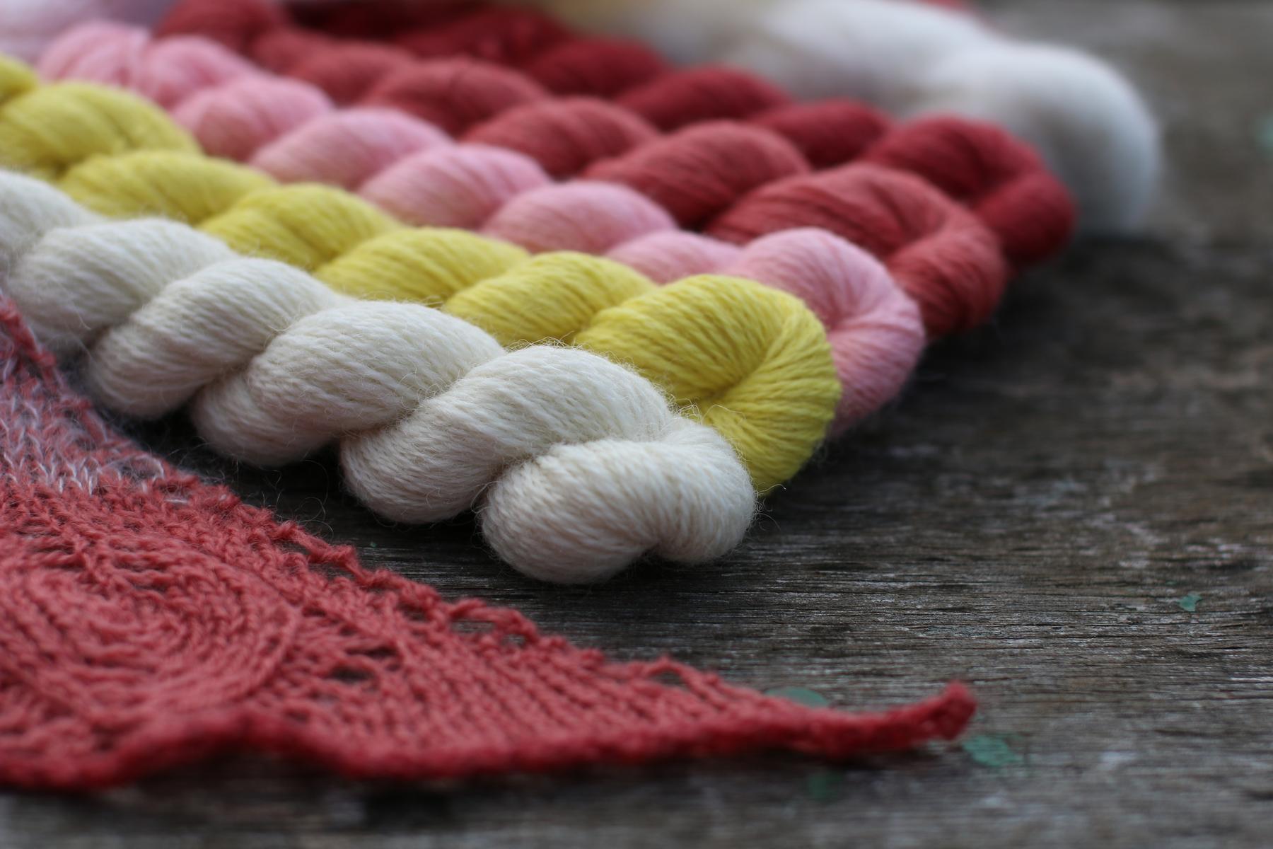 Several skeins of wool in a variety of colours, white, lemon, pink, and red