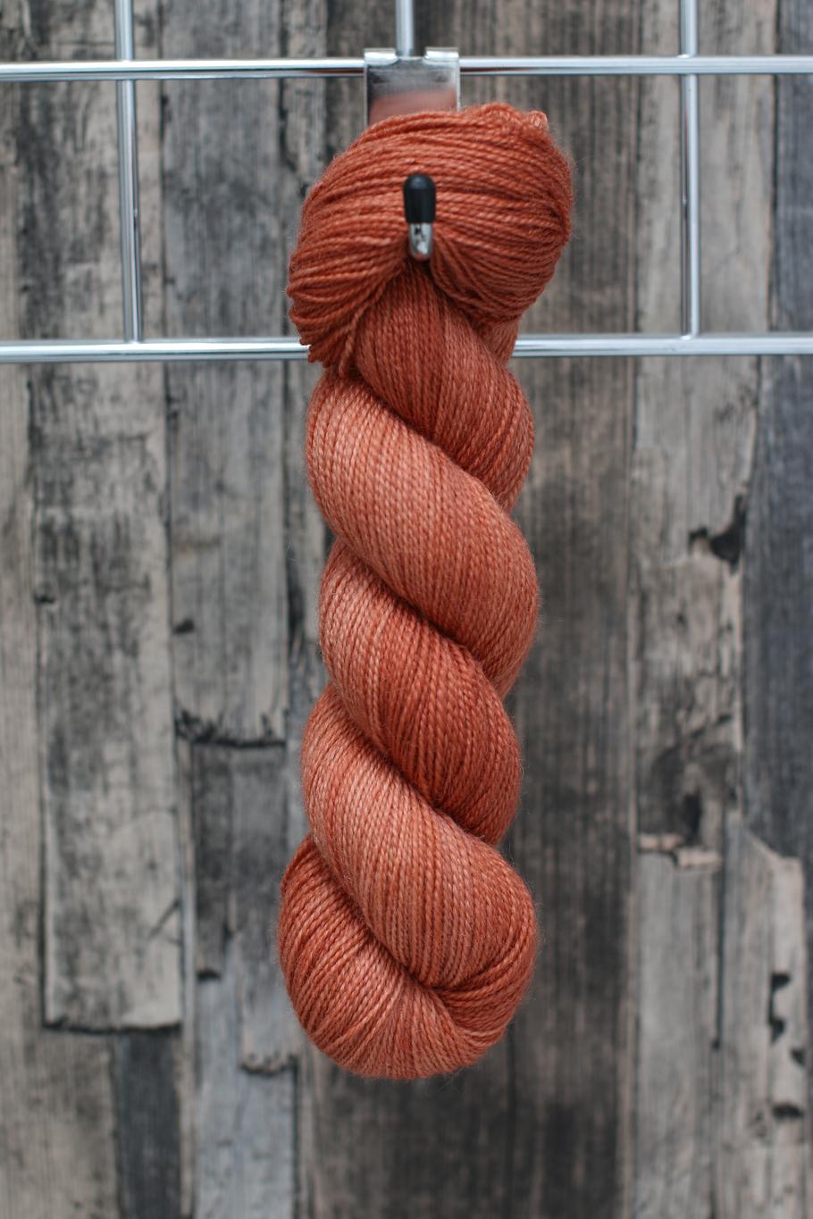 A single skein of yarn hanging from a hook in a variegated shade of soft orange