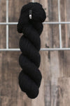 An almost black skein of wool hanging from a hook