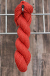 A single skein of light red wool hanging from a hook