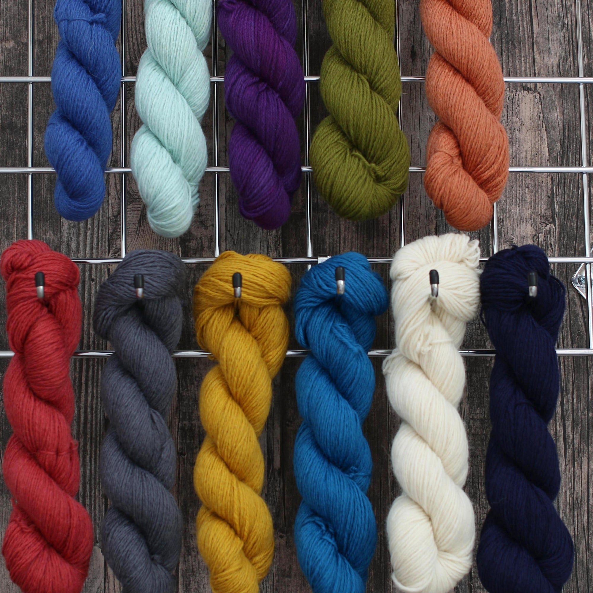 Eleven skeins of wool each a different colour, hanging from hooks on a wall