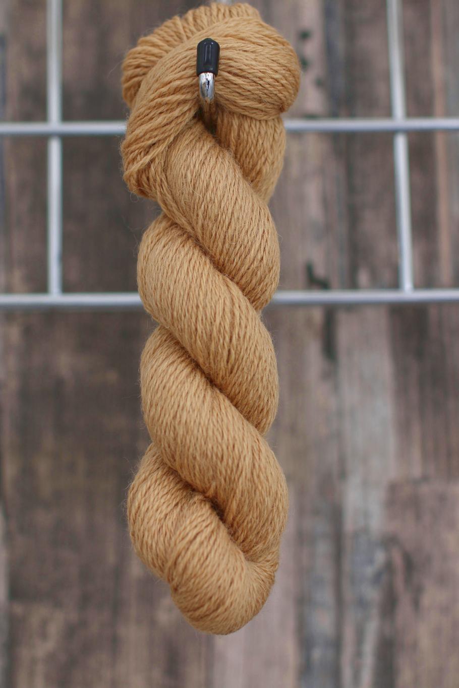 a single skein of camel coloured wool hanging from a hook