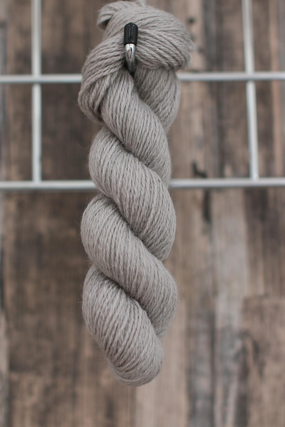 a single skein of light grey wool hanging from a hook