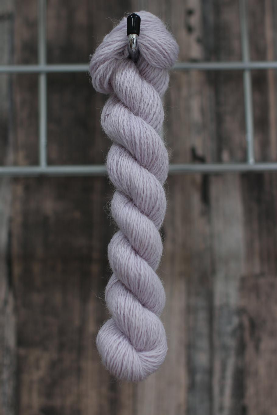A single skein of pale lavender wool hanging from a hook