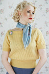 A woman wearing a knitted short sleeved lacy jumper in yellow, looking away from the camera